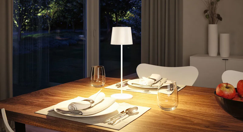 Moderne, kabellose Akku-Tischleuchte in weiß auf Holz-Esstisch